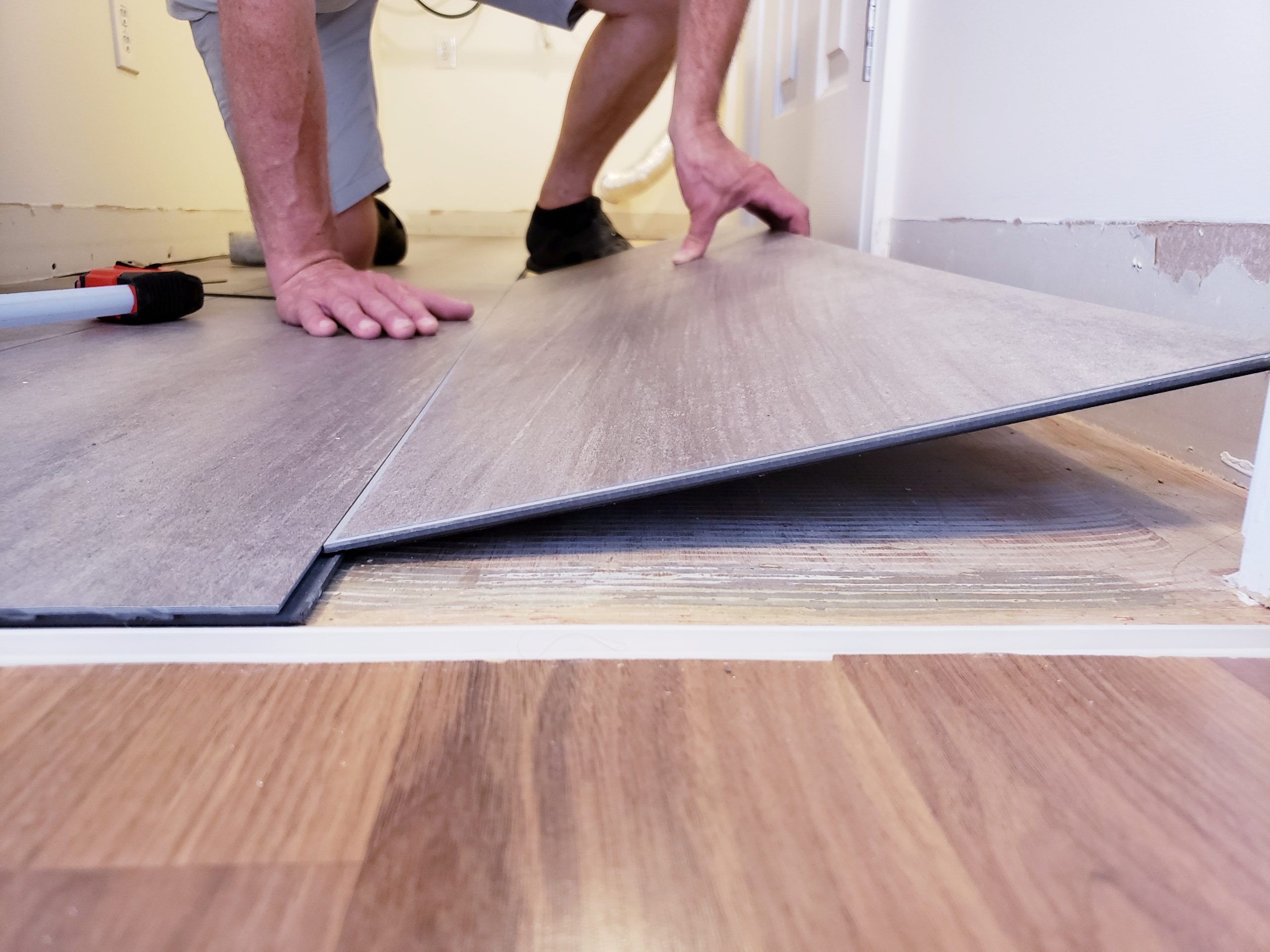 a man's arm as he lays down laminate flooring on a bare floor. The man is not visible.