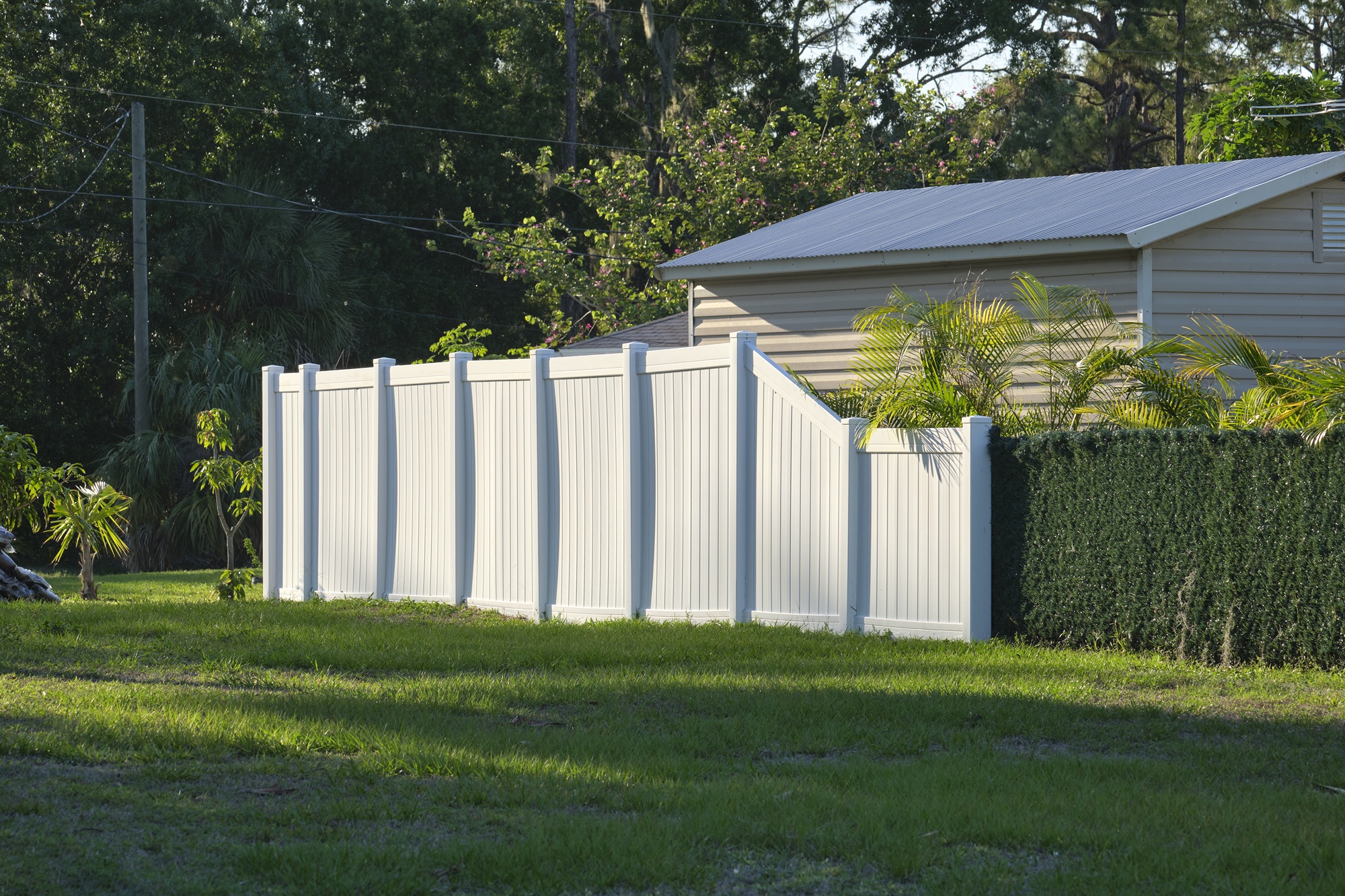 A white plastic fence on a lawn. The fence is multileveled and appears recently installed.